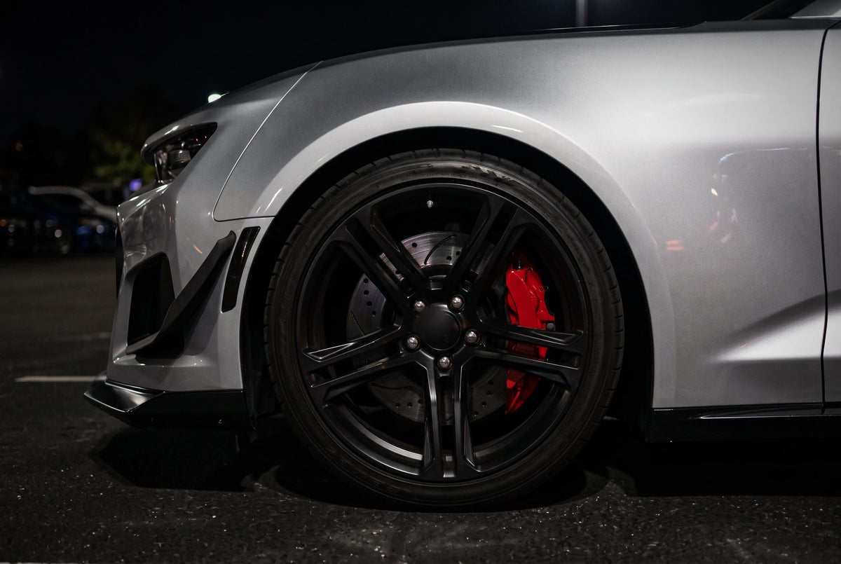 SP Performance double drilled and slotted brake rotor in black zinc with a red caliper, behind the wheel of a silver car at a night car meet