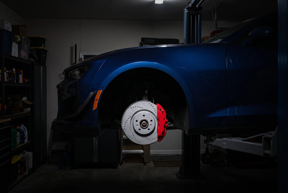 SP Performance cross drilled brake rotor in gray zinc with a red caliper, installed on a blue car on a garage lift