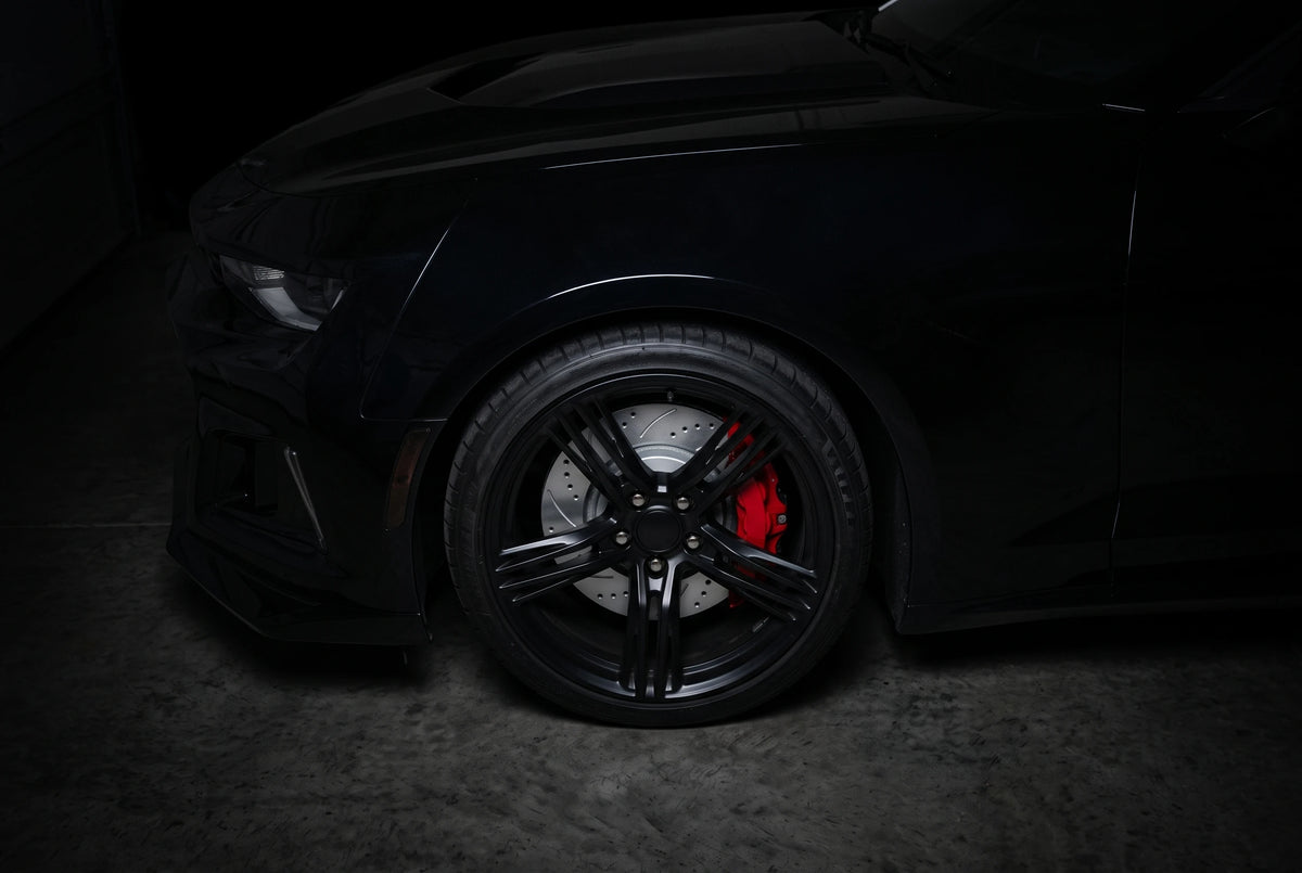 SP Performance double drilled and slotted brake rotor in gray zinc with a red caliper, behind the wheel of a black car in a dark garage