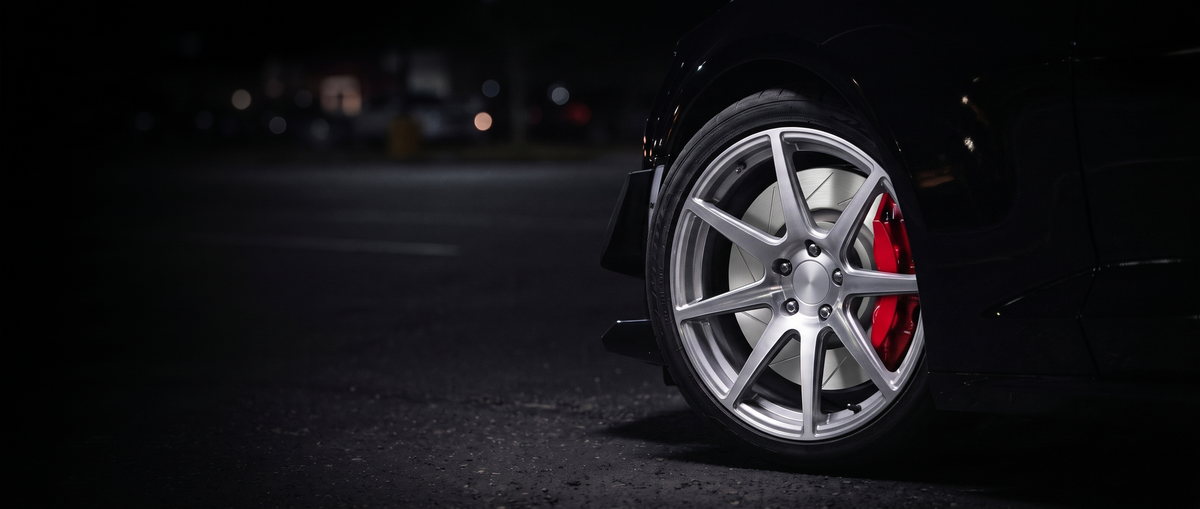 SP Performance slotted brake rotor in silver zinc with a red caliper, seen through the wheel of a car at night