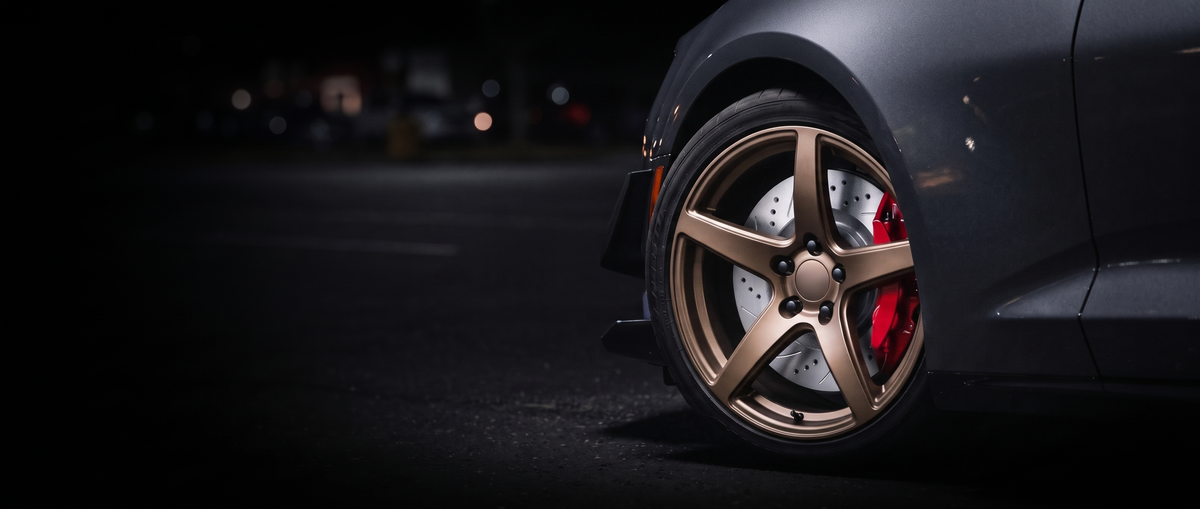 SP Performance cross drilled brake rotor in silver zinc with a red caliper, seen through the wheel of a car at night
