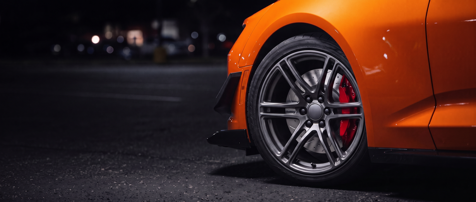 SP Performance drilled and slotted brake rotor in silver zinc with a red caliper, seen through the wheel of a car at night